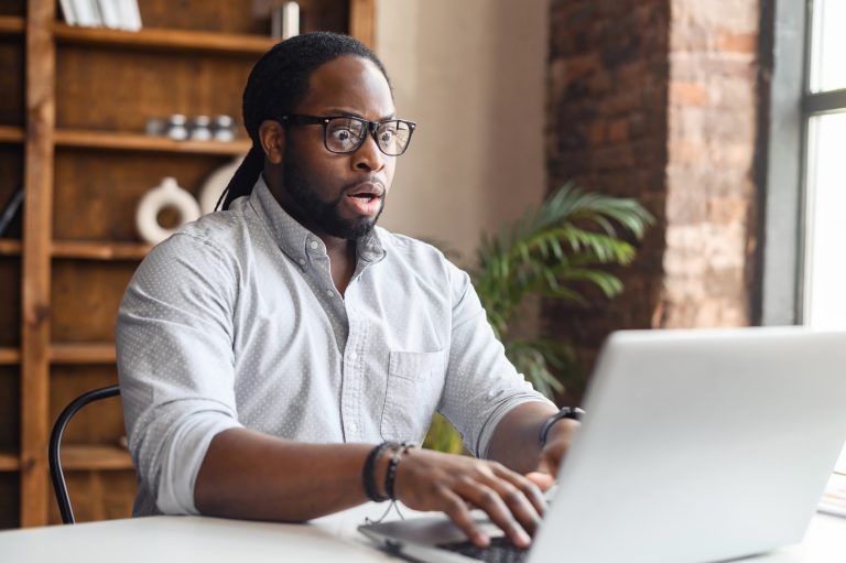 Upset business man working with laptop computer in office, feeling stressed and anxious for possible data loss. Adult Hispanic executive under stress at work for technology problems and software laptop surprised shocked upset stressed mental health wellness wellbeing