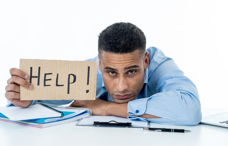 Desperate young attractive businessman working on computer laptop suffering stress at office going crazy holding a help sign. In stress at work, anxiety, technology problems and overwork concept. overworked needs help wellness wellbeing mental health