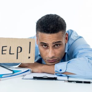 Desperate young attractive businessman working on computer laptop suffering stress at office going crazy holding a help sign. In stress at work, anxiety, technology problems and overwork concept. overworked needs help wellness wellbeing mental health