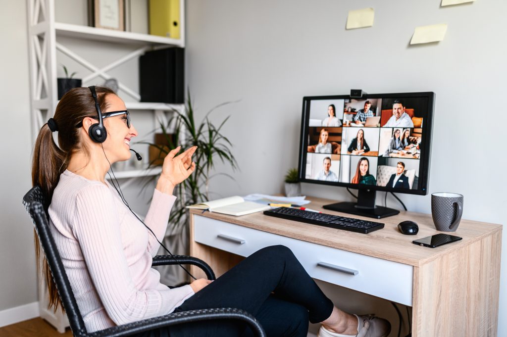 Young successful employee is have a meeting with her team using a headset, she is sitting relaxed and smiling, a middle side shot virtual online