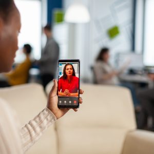 Over the shoulder of employee discussing with team member on video call using phone in start up business office. woman during video meeting, online conference planning new financial project