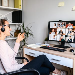 Young successful employee is have a meeting with her team using a headset, she is sitting relaxed and smiling, a middle side shot virtual online