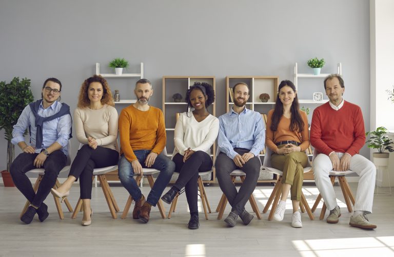 Happy diverse audience sitting on row of chairs during event in modern office room