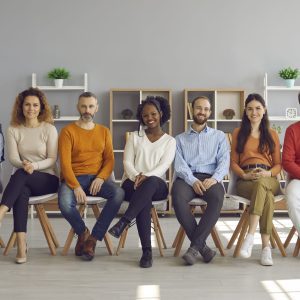 Happy diverse audience sitting on row of chairs during event in modern office room