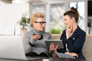 Happy young woman talking with her senior mentor Senior woman talking with young businesswoman, using digital tablet, sharing experience, senior women menopause