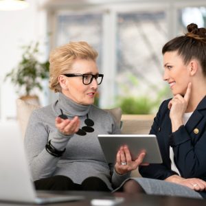 Happy young woman talking with her senior mentor Senior woman talking with young businesswoman, using digital tablet, sharing experience, senior women menopause