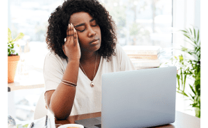 headache tired employee female sitting at her desk stressed overwhelmed cannot focus struggle timelines deadlines