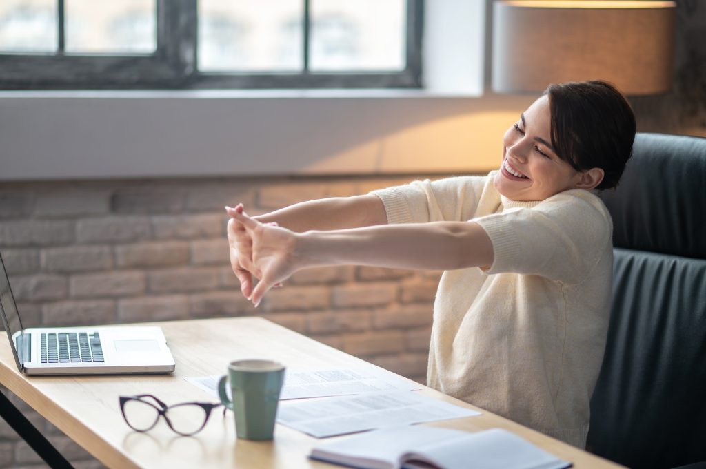 pleased female employee doing wrist stretches desk