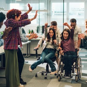 Young diverse business people racing in an office chair race at work having fun and enjoying themselves in the workplace to create a happy work culture and productive teams that work together to achieve success team work creativity