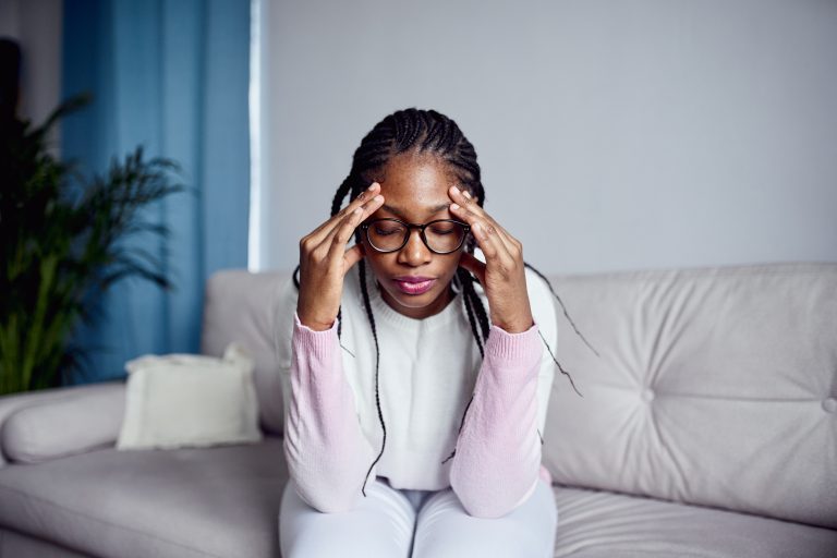 A young girl is sitting on the couch at home with her head in her hands GettyImages-1356562872 - Medihelp - stress well-being wellbeing wellness burnout tired