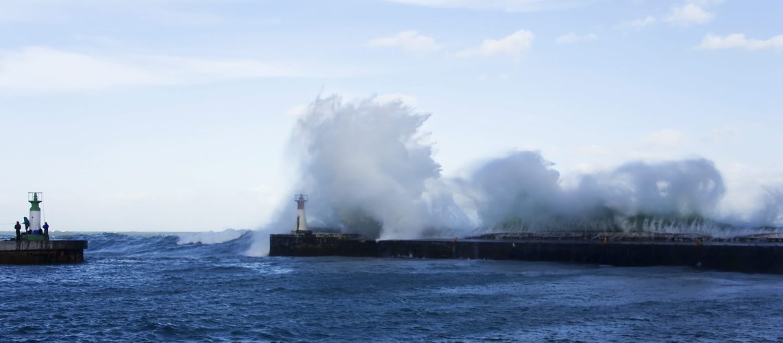 Waves crashing over lighthouse in Kalk Bay Harbour as fishermen brave storm, Cape Town, South Africa.