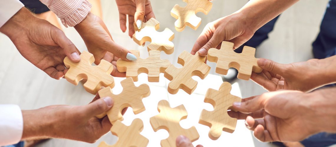 Close up of company workers finding solution in corporate work meeting. Cropped office employees learning to collaborate and playing with pieces of jigsaw puzzle during team building activity