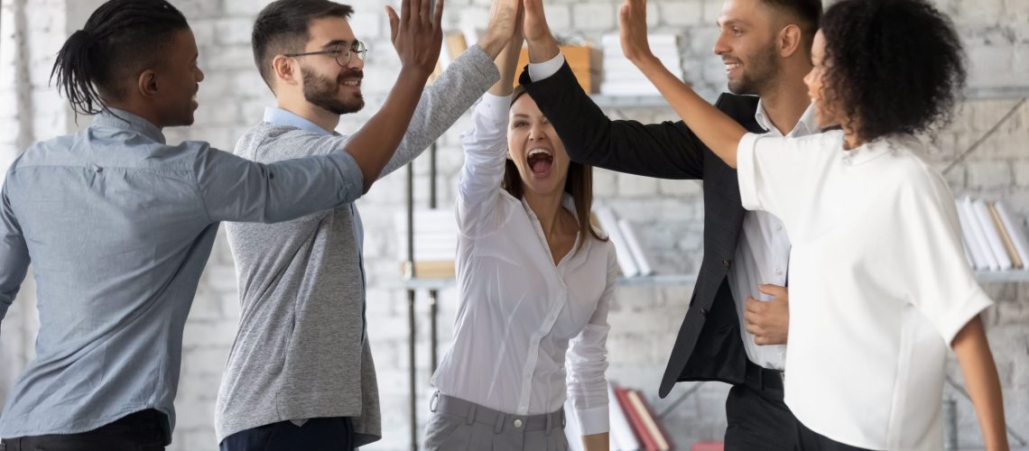 Excited successful multiracial business people giving high five, celebrating win. Good teamwork result concept. Happy employees team engaged in team building activity at corporate meeting.