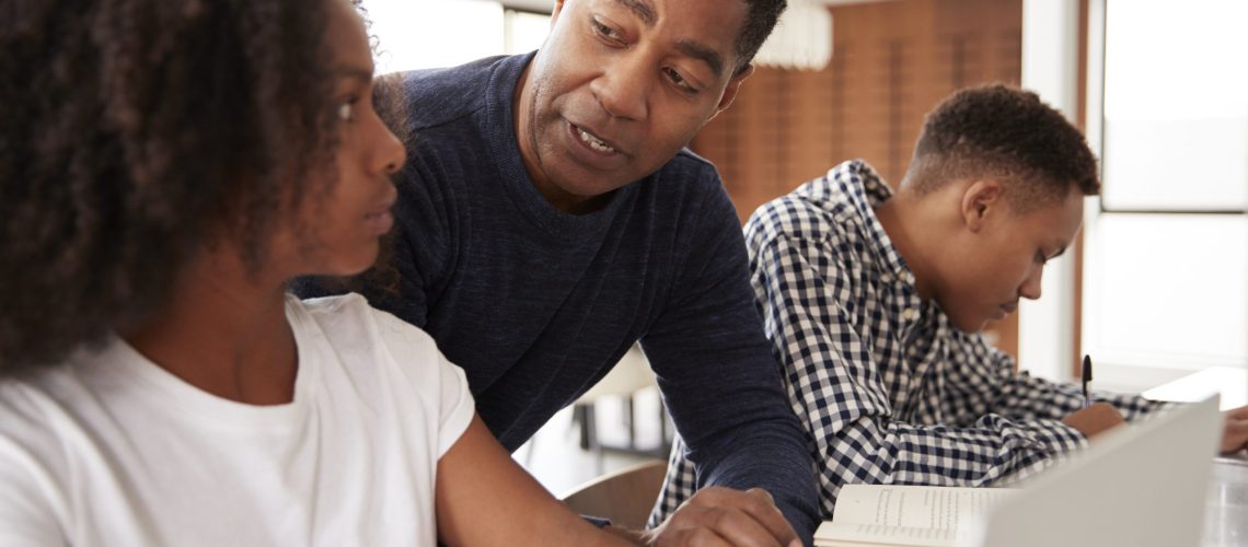 Middle aged black dad helping his teen kids with homework, low angle, close up