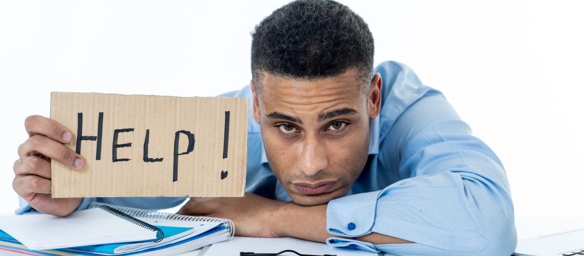 Desperate young attractive businessman working on computer laptop suffering stress at office going crazy holding a help sign. In stress at work, anxiety, technology problems and overwork concept. overworked needs help wellness wellbeing mental health