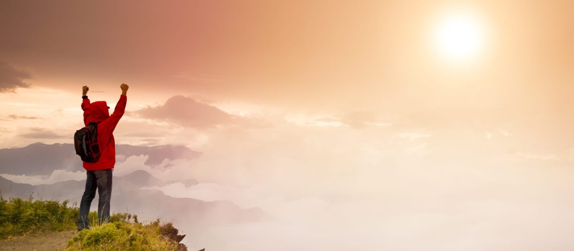 Young man with backpack standing  on top of  mountain watching the sunrise