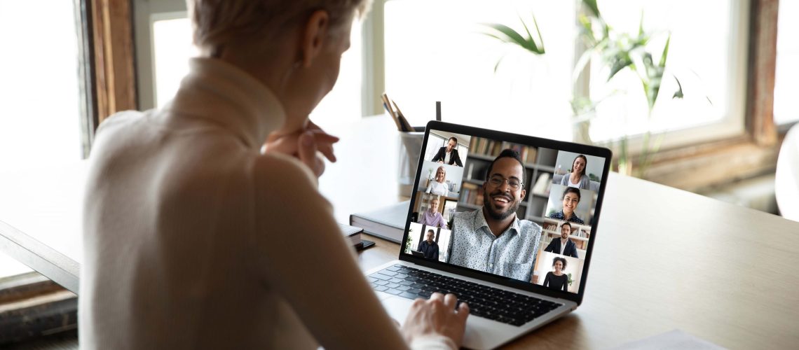 Woman sitting at workplace desk taking part at group on-line meeting using webcam laptop and videoconferencing app, view over female shoulder. Modern tech, distant webinar, online negotiations concept remote work engagement hr tech