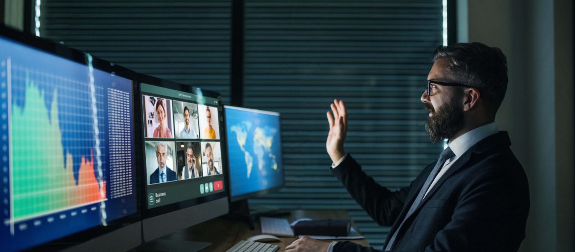 Businessman with computer sitting at desk, working late. Financial crisis and video call concept.