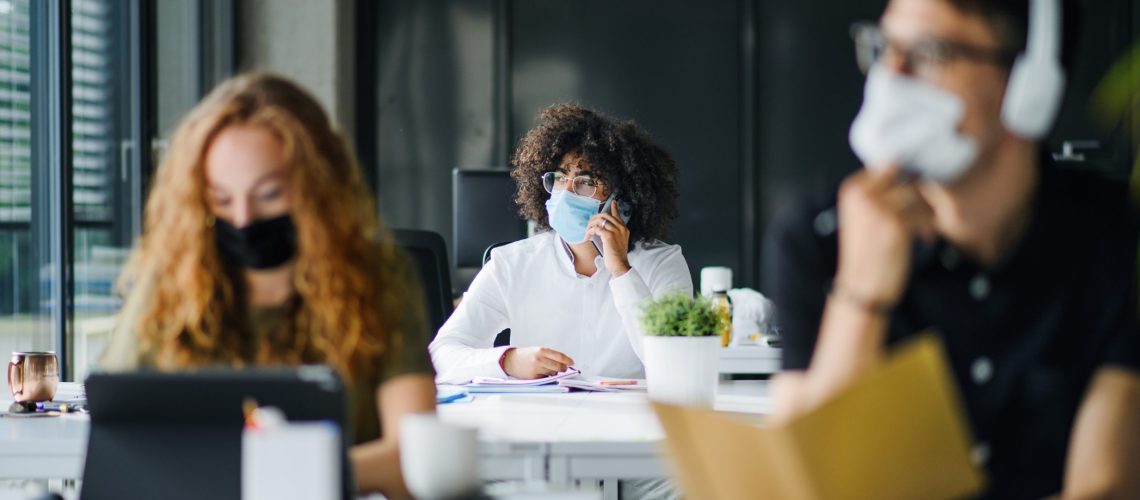 Young people with face masks back at work in office after coronavirus quarantine and lockdown.