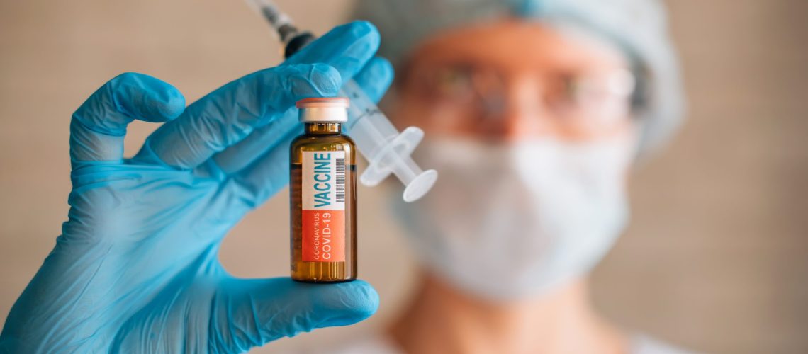 Blurred image: doctor holding syringe and coronavirus Covid-19 vaccine vial. Vaccination, pharmaceutical research concept.