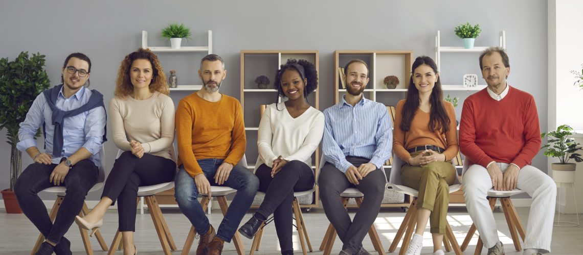 Happy diverse audience sitting on row of chairs during event in modern office room