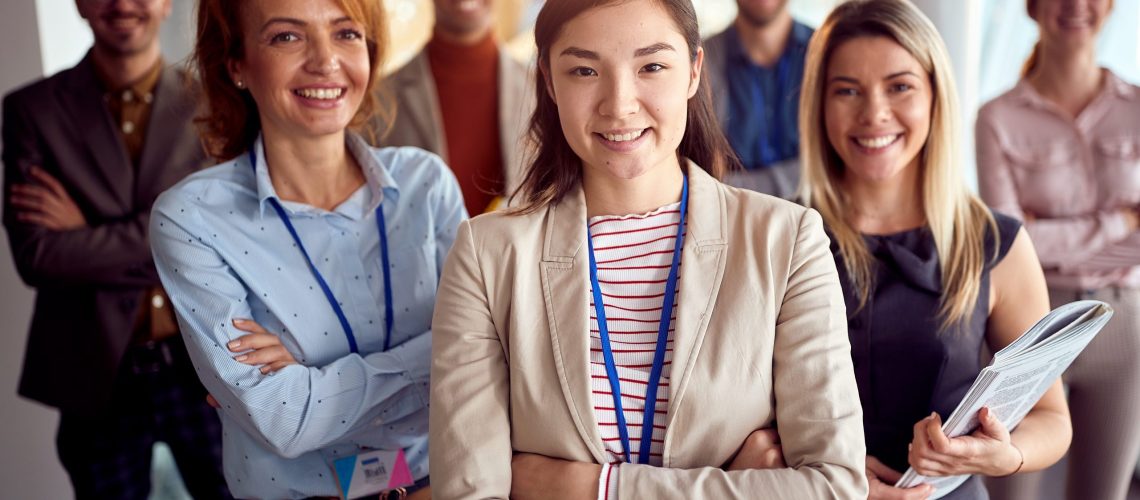 A young cheerful business woman is standing in a pleasant atmosphere in the company building hallway with her colleagues and enjoys posing for a photo. Business, people, company