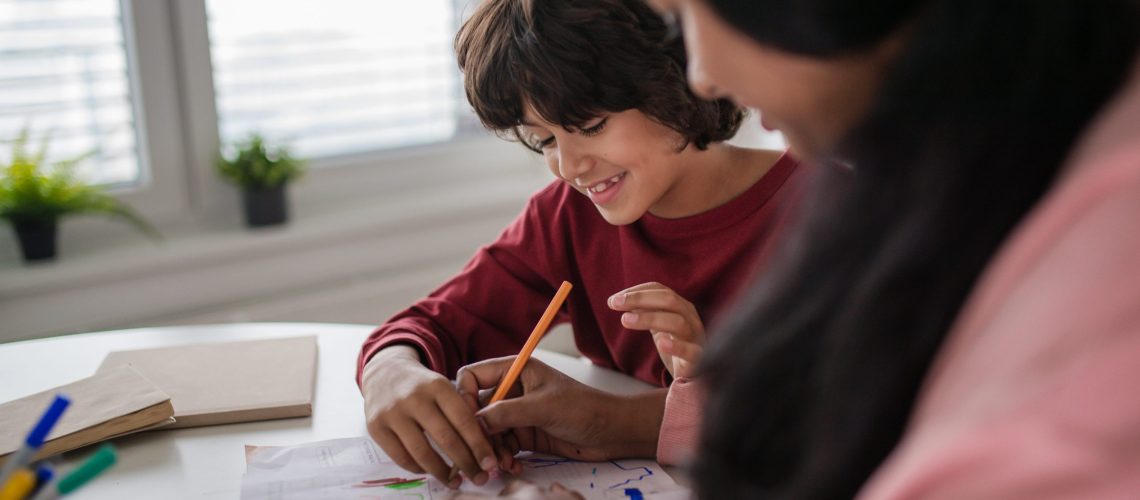 A little multiracial boy doing homework with his mother at home.