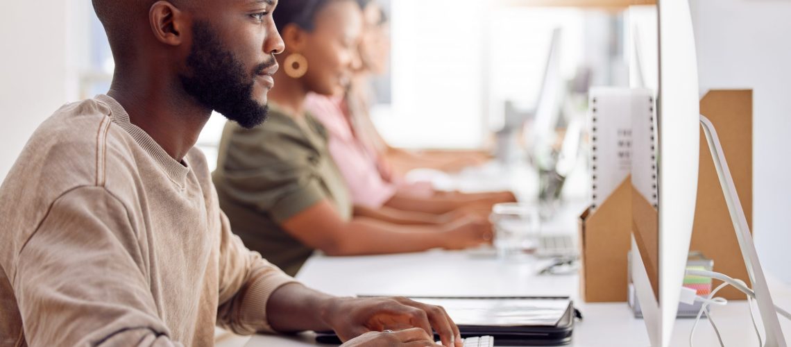 Shot of a businessman working on his computer while his colleagues sit in the background