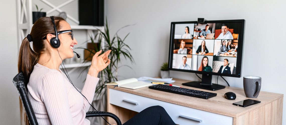 Young successful employee is have a meeting with her team using a headset, she is sitting relaxed and smiling, a middle side shot virtual online