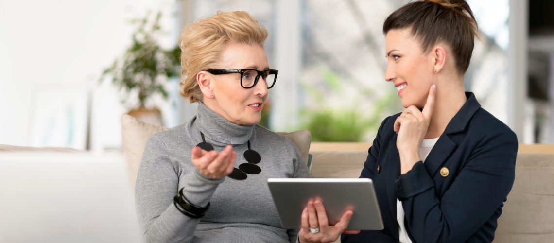 Happy young woman talking with her senior mentor Senior woman talking with young businesswoman, using digital tablet, sharing experience, senior women menopause