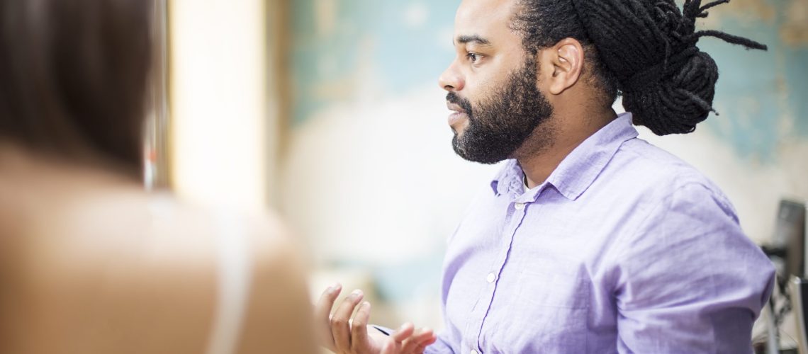 Young African American man talking something to other young people in the office