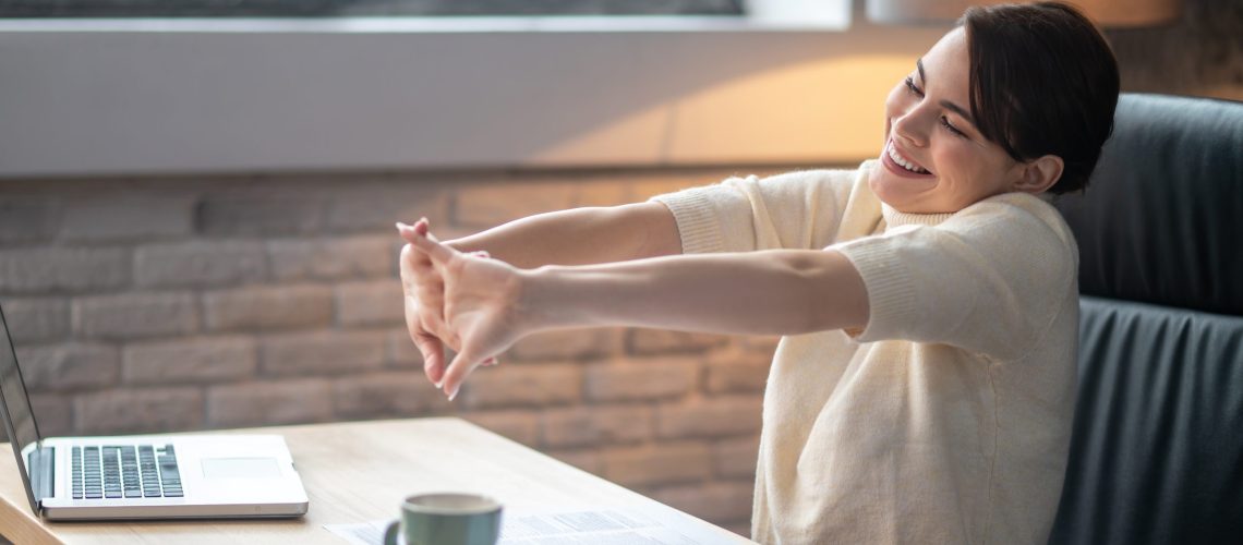 Pleased female doing wrist stretches at the desk health wellness wellbeing ergonomics productive